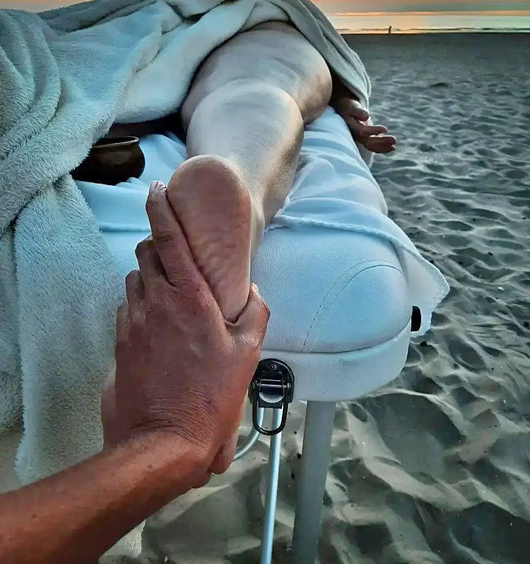 Een massage aan zee bij zonsondergang: Ellens hand rust op een voet
