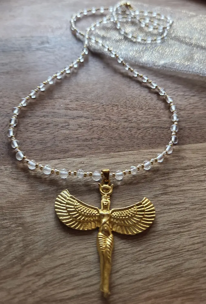 Ketting met doorzichtige kralen en een gouden hanger met vleugels, op hout