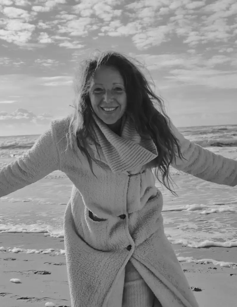Ellen op het strand met haar armen wijd, lachend, de zee achter haar