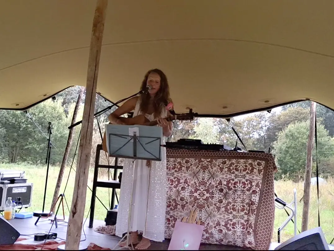 Ellen zingt met haar gitaar onder een tentdoek, buiten in het groen
